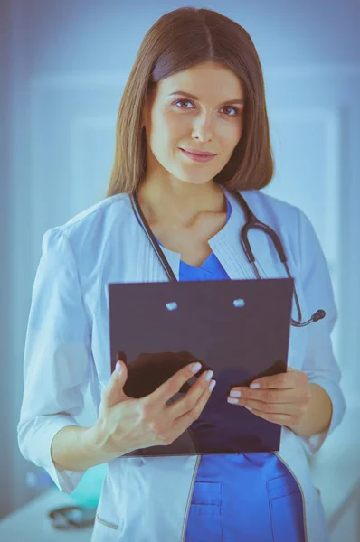 Doctora de pie con una carpeta en las manos en el hospital, sonriendo a la cámara — Foto de Stock