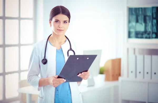 Joven doctora sonriente con estetoscopio sosteniendo una carpeta en el consultorio médico — Foto de Stock