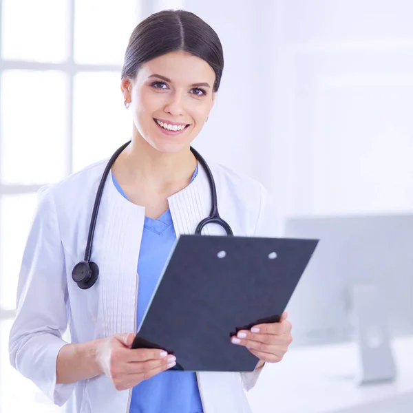Young smiling female doctor with stethoscope holding a folder at a hospitals consulting room Stock Image