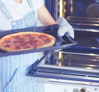 Mutlu genç bayan evde pizza pişiriyor.