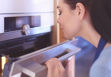Güzel genç bayan pastasının fırında ne yaptığını kontrol ediyor.