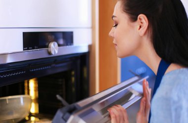 Güzel genç bayan pastasının fırında ne yaptığını kontrol ediyor.
