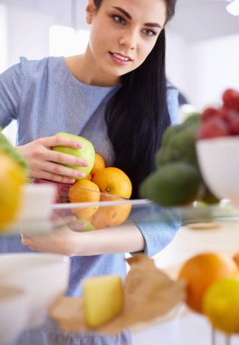 Gülümseyen kadın buzdolabından taze meyve alıyor, sağlıklı yiyecek konsepti.