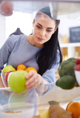 Gülümseyen kadın buzdolabından taze meyve alıyor, sağlıklı yiyecek konsepti.