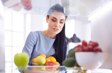 Gülümseyen kadın buzdolabından taze meyve alıyor, sağlıklı yiyecek konsepti.
