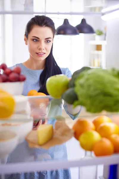 Mulher sorridente tirando uma fruta fresca da geladeira, conceito de comida saudável — Fotografia de Stock