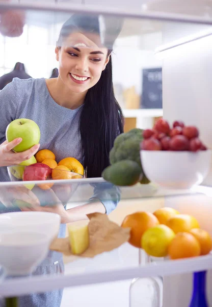 Smiling woman taking a fresh fruit out of the fridge, healthy food concept — Stock Photo, Image