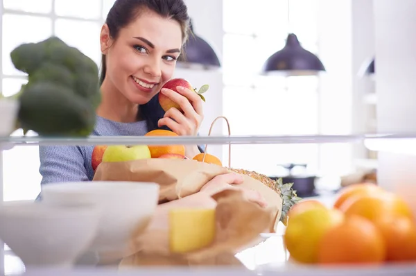 Χαμογελώντας γυναίκα λαμβάνοντας ένα φρέσκο φρούτο από το ψυγείο, έννοια υγιεινής διατροφής — Φωτογραφία Αρχείου