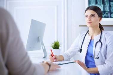 Doktor ve hasta hastane danışma odasında tıbbi sorunları tartışıyorlar. Doktor hasta formunu dolduruyor.