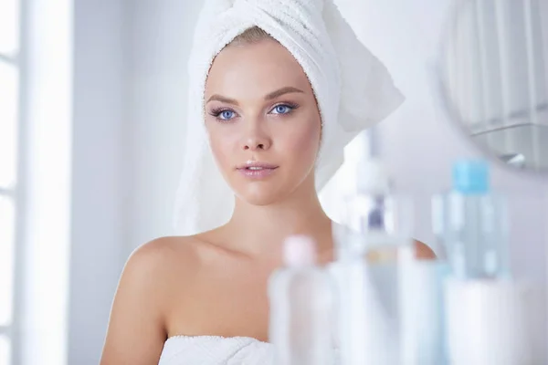 Young woman in bathrobe looking in bathroom mirror — Stock Photo, Image