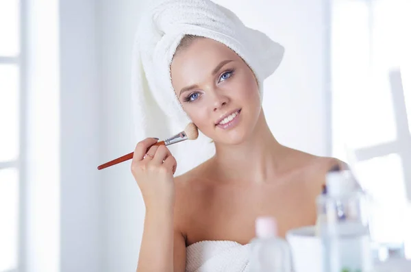 Una foto de una mujer joven aplicando polvo facial en el baño — Foto de Stock