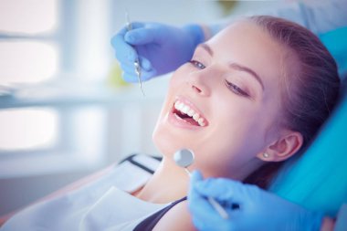 Dişçi muayenehanesinde diş muayenesi yapan ağzı açık genç bir kadın hasta..