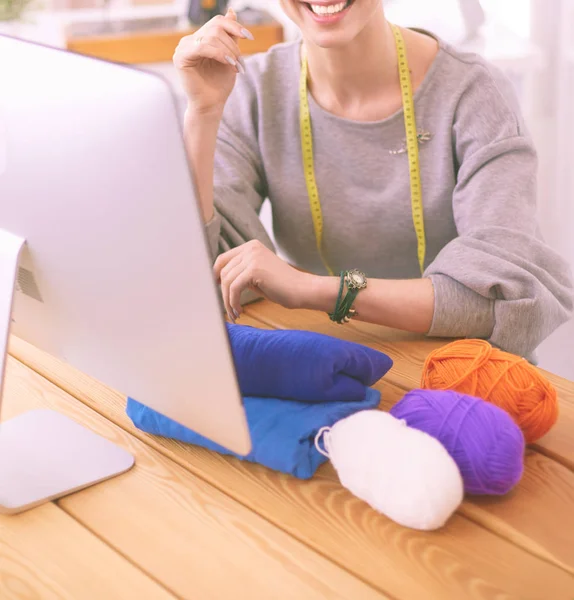 Een portret van een jonge ontwerper vrouw met behulp van een laptop en glimlachend, kleren opgehangen als achtergrond — Stockfoto