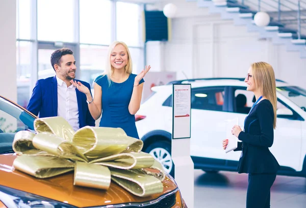 Een man maakt een geschenk - een auto aan zijn vrouw. Ze is hier verbaasd over. Ze zijn hier erg blij mee. — Stockfoto
