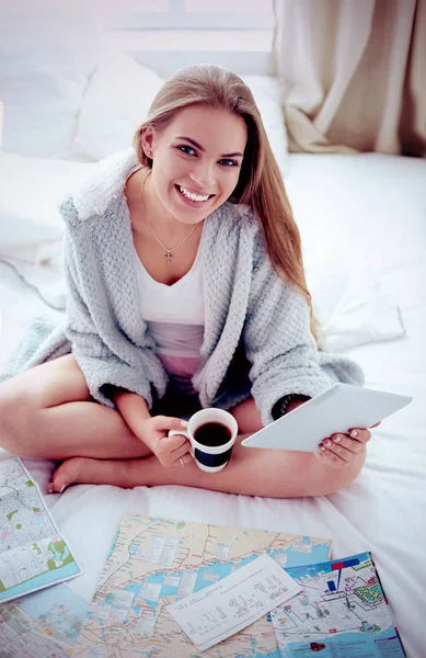 Relaxado jovem mulher sentada na cama com uma xícara de café e tablet digital — Fotografia de Stock