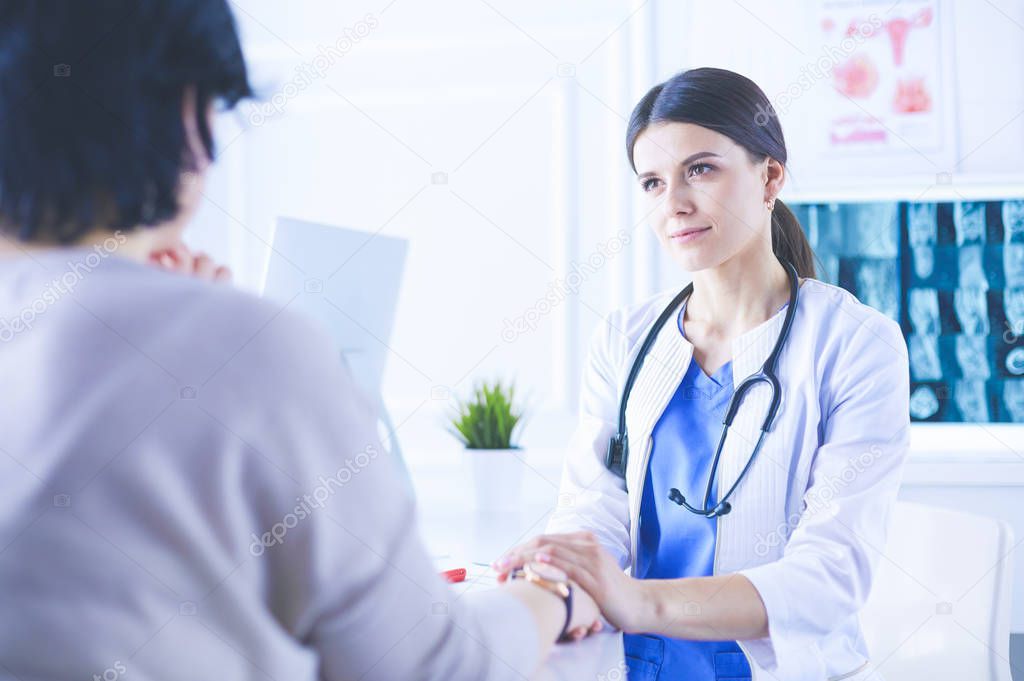 Female doctor calming down a patient at a hospital consulting room, holding her hand