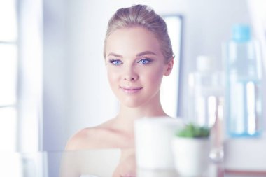 Bornozlu genç kadın banyo aynasına bakıyor.