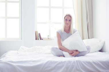 sevimli kadın yatağında otururken bir yastık holding