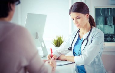 Doktor ve hasta hastane danışma odasında tıbbi sorunları tartışıyorlar. Doktor hasta formunu dolduruyor.