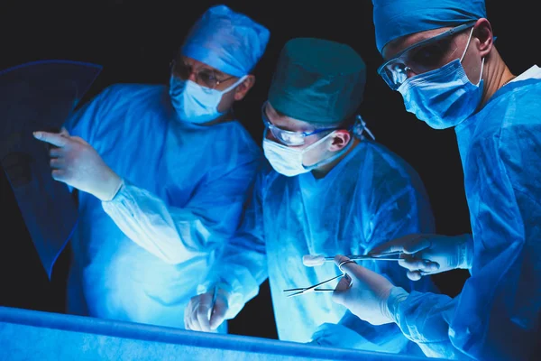 Group of surgeons at work in operating theater toned in blue. Medical team performing operation — Stock Photo, Image