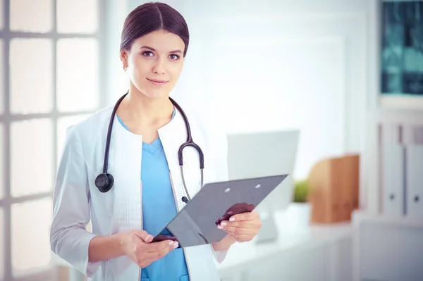 Joven doctora sonriente con estetoscopio sosteniendo una carpeta en el consultorio médico — Foto de Stock