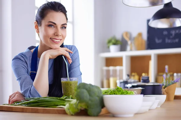 Mujer joven con vaso de sabroso batido saludable en la mesa en la cocina —  Fotos de Stock