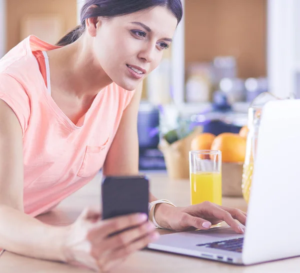 Vacker kvinna på telefon med bärbar dator hemma i köket — Stockfoto