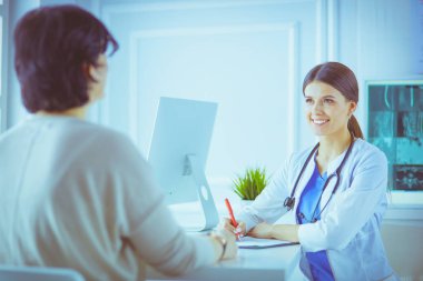 Doktor ve hasta hastane danışma odasında tıbbi sorunları tartışıyorlar. Doktor hasta formunu dolduruyor.