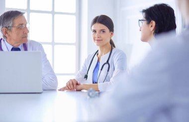 Ciddi bir tıbbi ekip, parlak bir danışma odasında dizüstü bilgisayar kullanıyor.