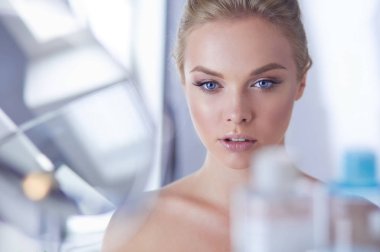 Bornozlu genç kadın banyo aynasına bakıyor.