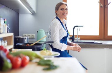 Mutfakta sobanın yanında duran genç bir kadın.