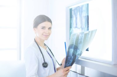 Doktor muayenehanesinde röntgene bakan steteskoplu, gülümseyen genç bayan doktor.