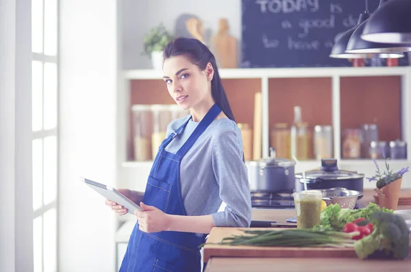 Jovem usando um computador tablet para cozinhar em sua cozinha — Fotografia de Stock