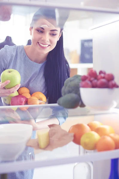 Mulher sorridente tirando uma fruta fresca da geladeira, conceito de comida saudável — Fotografia de Stock