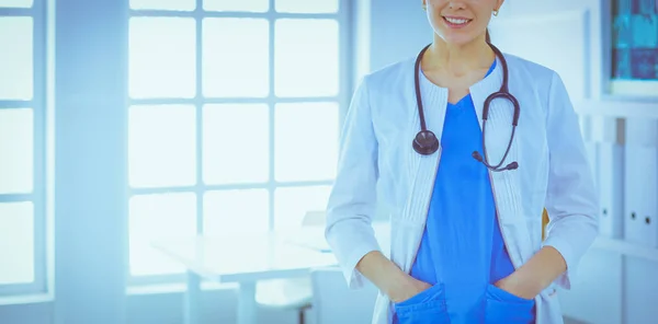 Médica de pé com estetoscópio e as mãos nos bolsos do hospital — Fotografia de Stock