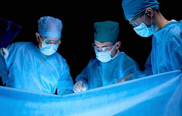 Grupo de cirujanos trabajando en quirófano tonificado en azul. Equipo médico realizando la operación — Foto de Stock