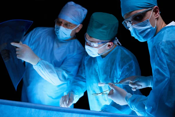 Grupo de cirurgiões no trabalho em sala de operações tonificada em azul. Equipe médica realizando operação — Fotografia de Stock