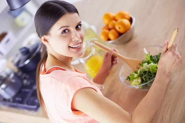 Smiling young woman mixing fresh salad in the kitchen. — Stock Photo, Image