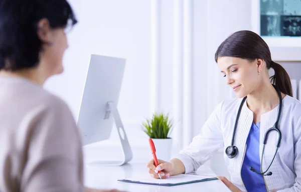 Dokter en patiënt bespreken medische problemen in een ziekenhuis spreekkamer. Doc vult een patiëntenformulier in — Stockfoto