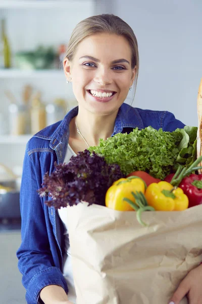 Jeune femme tenant sac d'épicerie avec des légumes. Debout dans la cuisine — Photo