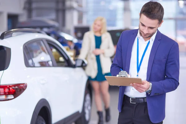 Vendedor fica perto de um carro novo no showroom — Fotografia de Stock