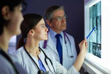 Bir grup doktor bir klinikte röntgenleri inceliyor, teşhis koymayı düşünüyorlar.