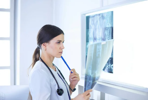 Νεαρή γυναίκα γιατρός με στηθοσκόπιο που εξετάζει ακτινογραφία στο ιατρείο — Φωτογραφία Αρχείου