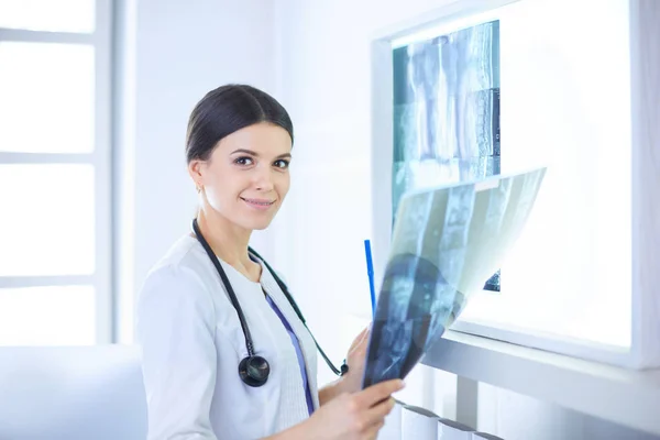 젊은 여성 의사가 청진기를 들고 웃으면서 의사 사무실에서 엑스레이를 보고 있는 모습 — 스톡 사진
