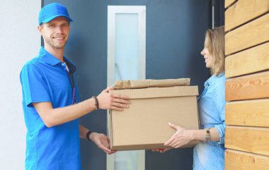 Mavi üniformalı gülümseyen kurye servis konseptine paket kutusu teslim eden teslimatçı.