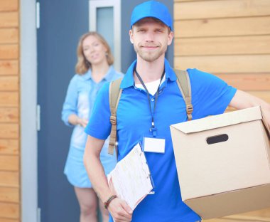 Mavi üniformalı gülümseyen kurye servis konseptine paket kutusu teslim eden teslimatçı.