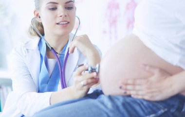 Smiling woman doctor shows pictures on the tablet to pregnant young woman at hospital. clipart