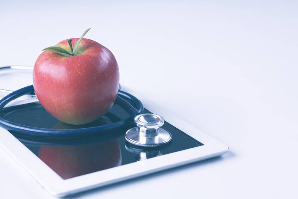 Medical stethoscope and red apple lying on a tablet isolated on white background.