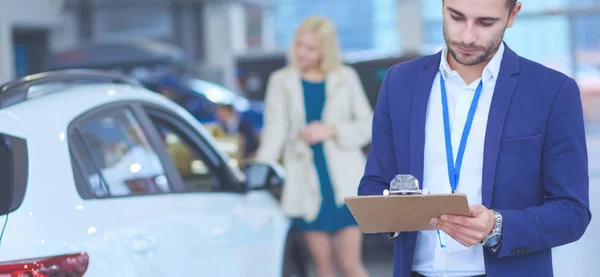 Distribuidor de mujer se para cerca de un coche nuevo en la sala de exposición — Foto de Stock