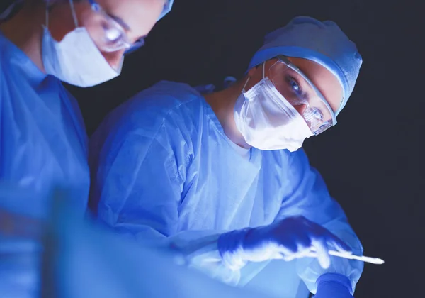 Equipo de médicos en cirugía en un fondo oscuro. — Foto de Stock